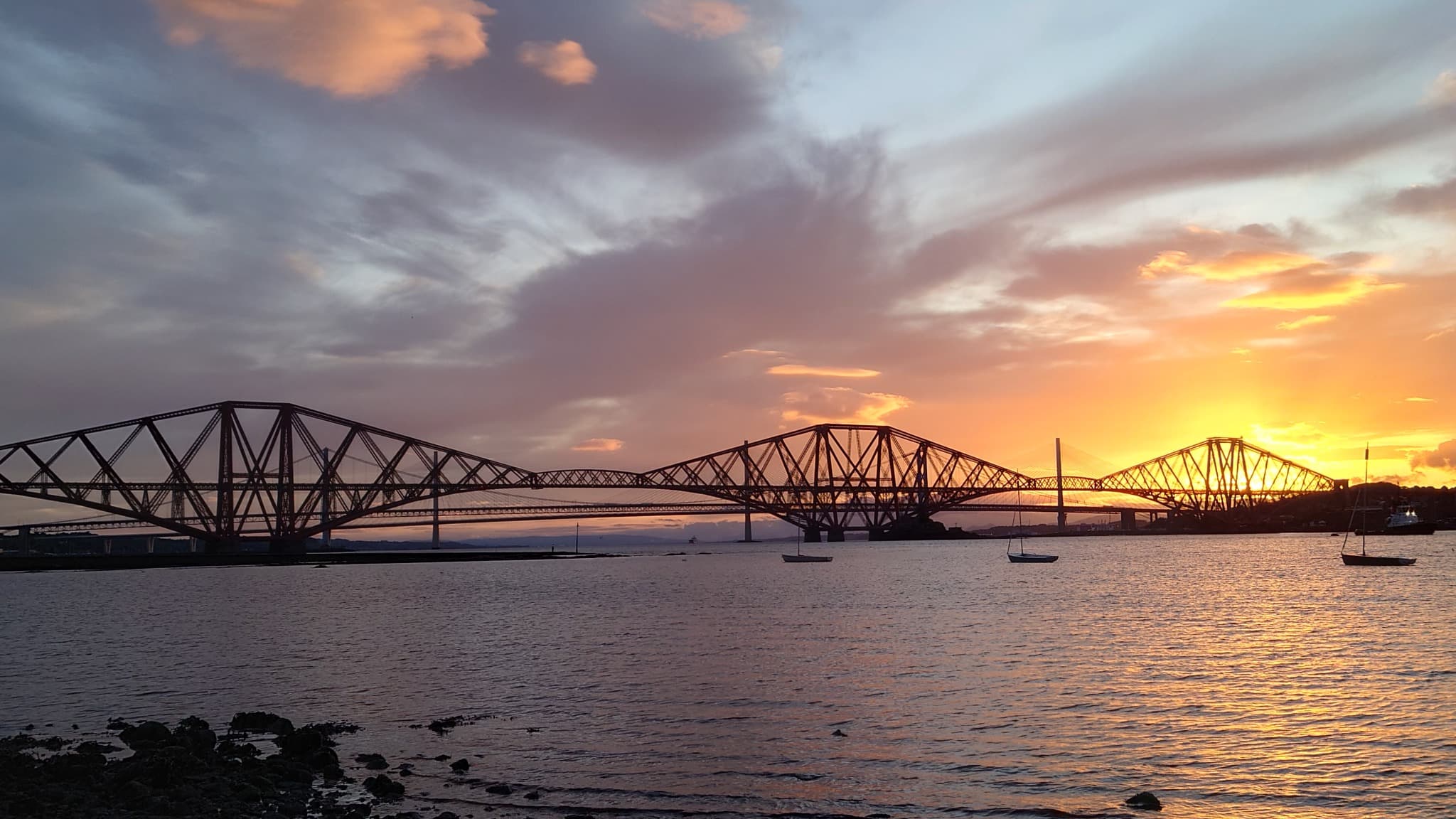 The Forth Bridge and nearby road bridges at sunset over the Firth of Forth near Edinburgh.